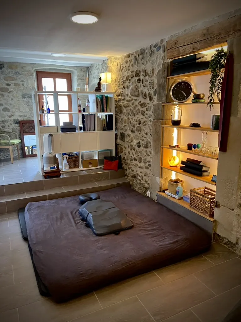 Cabinet de Shiatsu Olivier Larue au Grand-Lancy : futon de shiatsu, mur en pierre et étagères éclairées